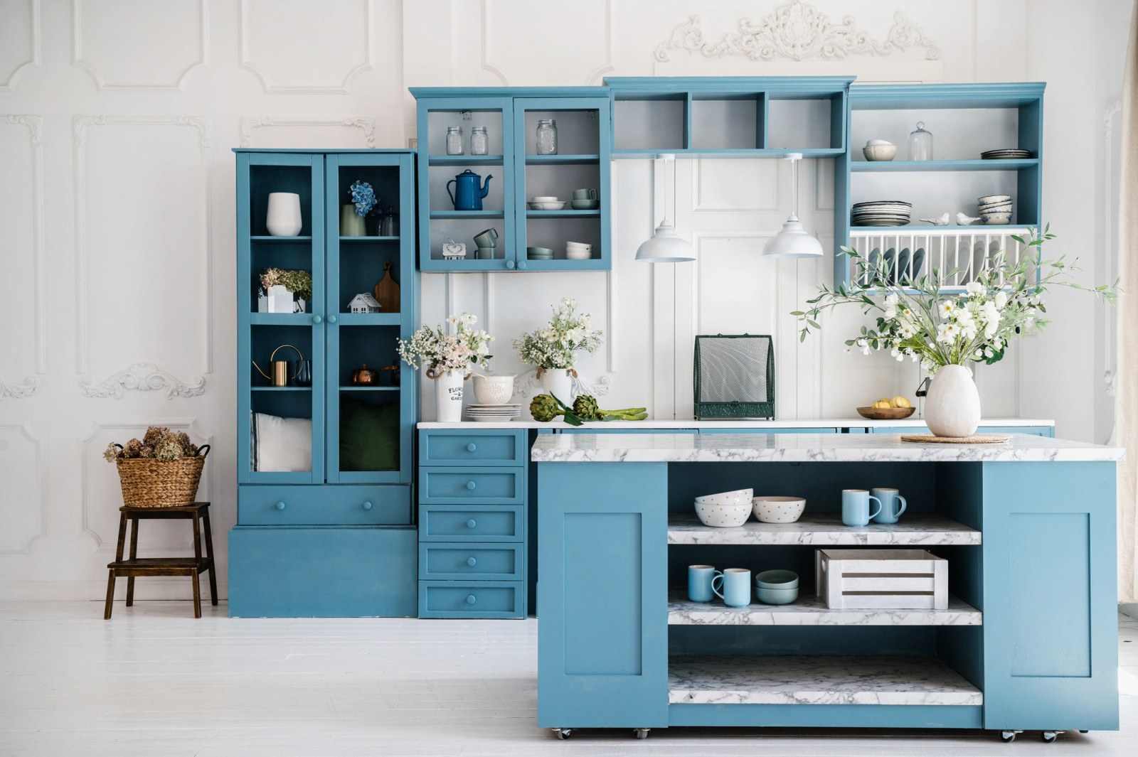 Blue painted kitchen cabinetry with a marble topped island against panelled white walls