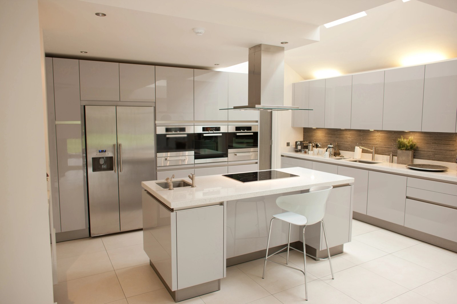 Handleless high gloss kitchen with an island, integrated hob and a glass and steel extractor hood