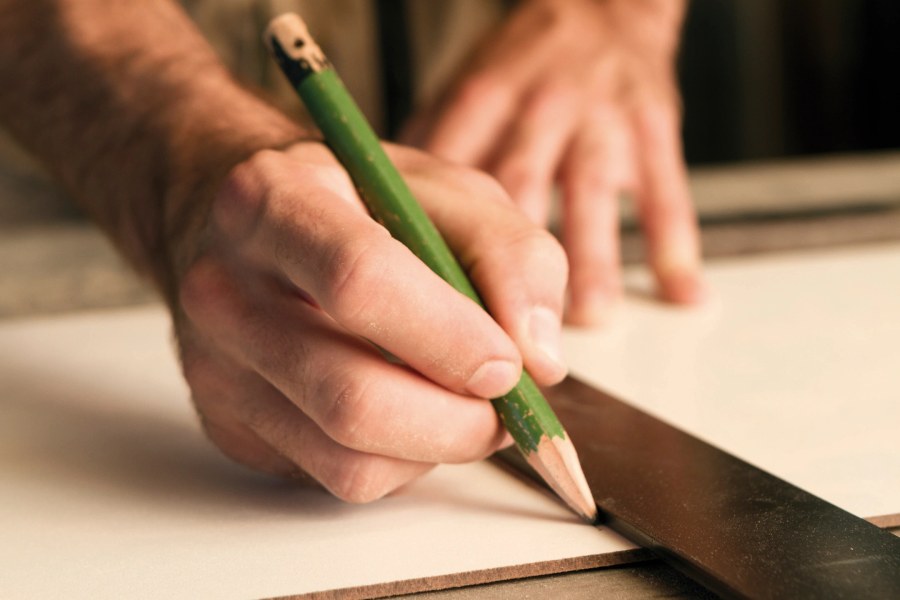 Installer marking a cut line on stone with a pencil and straight edge
